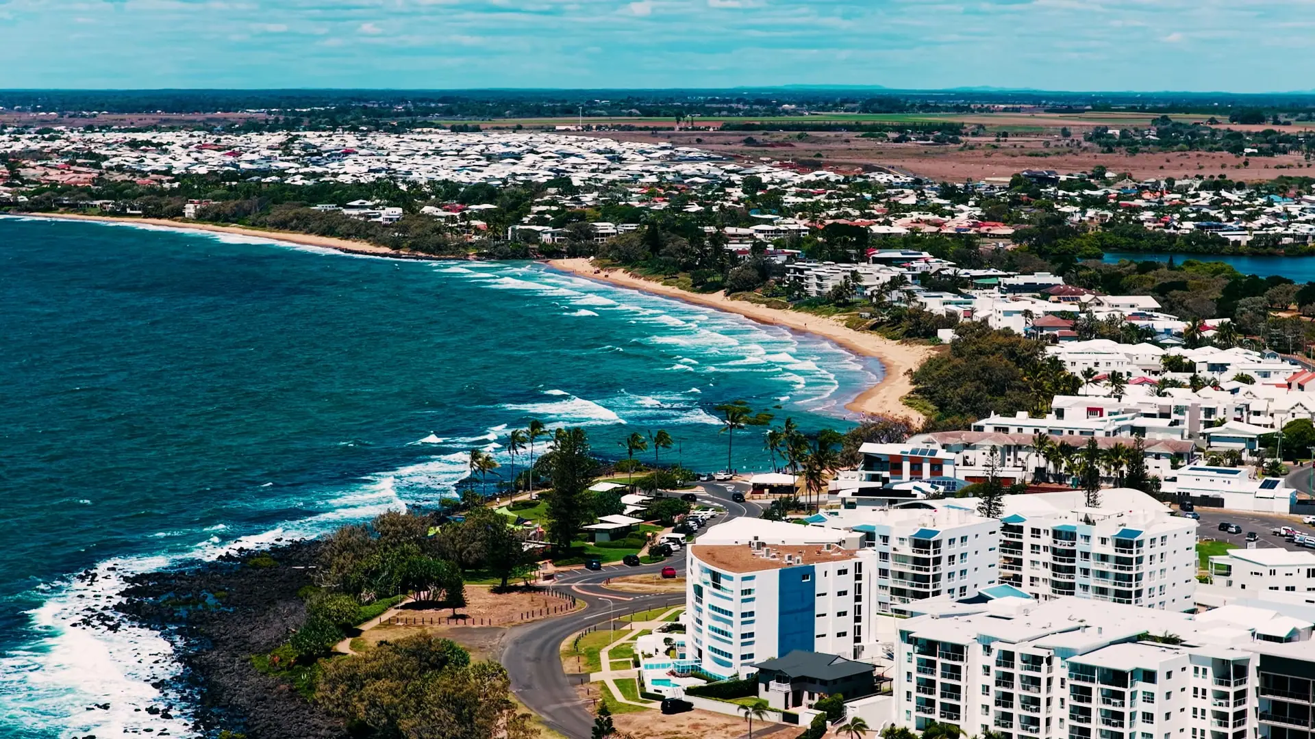 The Bargara coastline from the air: the beach curving towards the village, with the cane fields beyond
